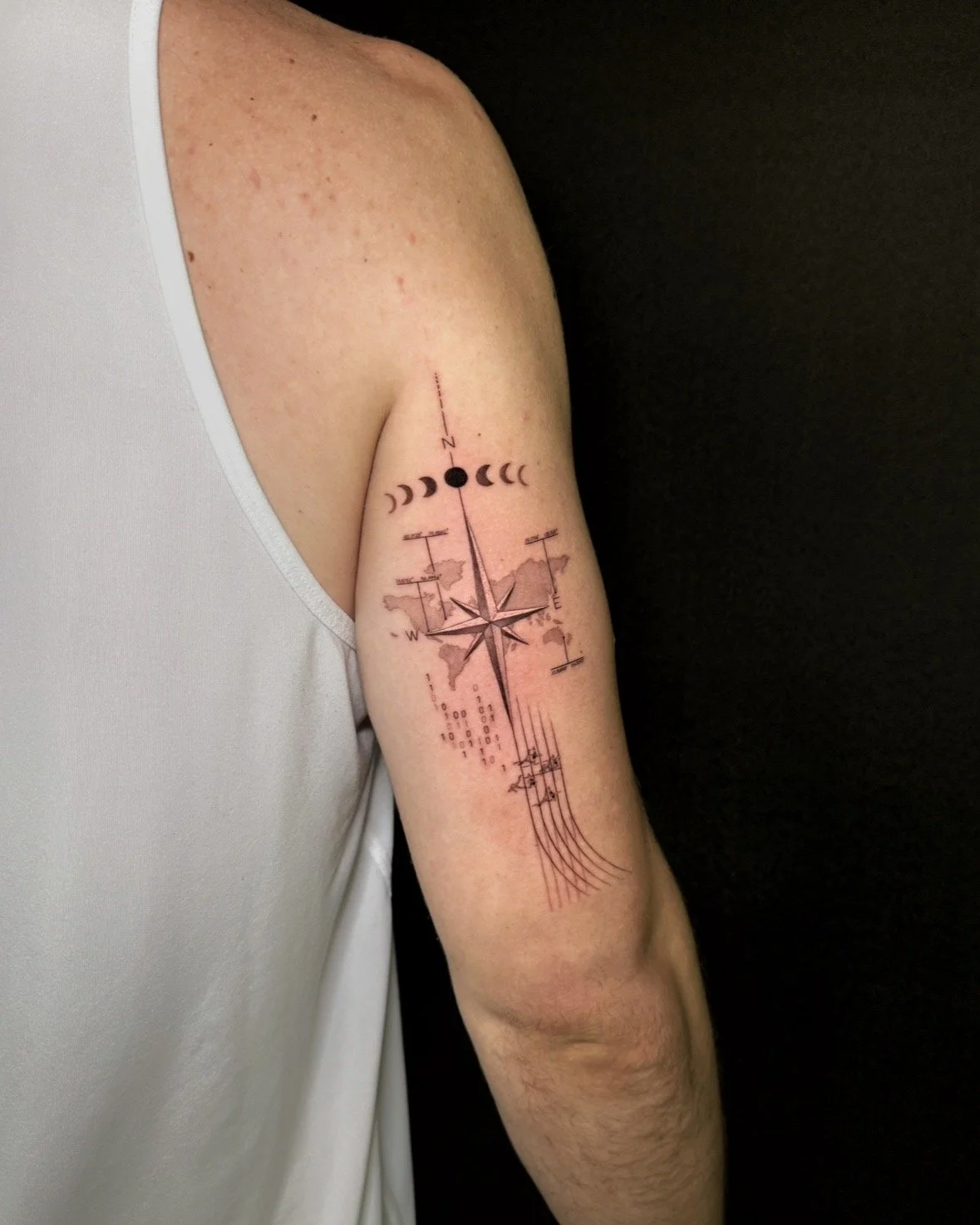A hyper realistic tattoo done by Ihor (flowerhead.ink) on person's triceps. Featuring a compass, world map, moon phases, binary code runners on a track. 