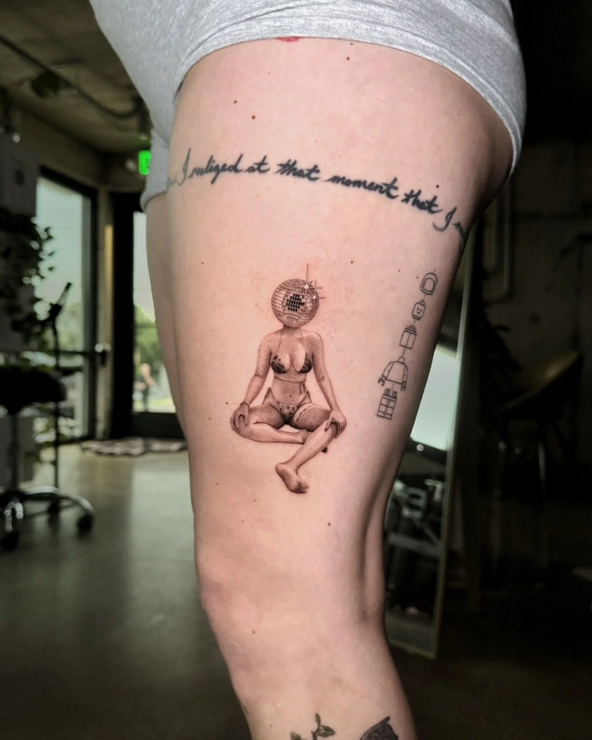 A hyper realistic tattoo done by Ihor (flowerhead.ink) on person's thigh. Featuring a self-portrait of a woman with a disco ball head, sitting cross-legged in a yoga pose.