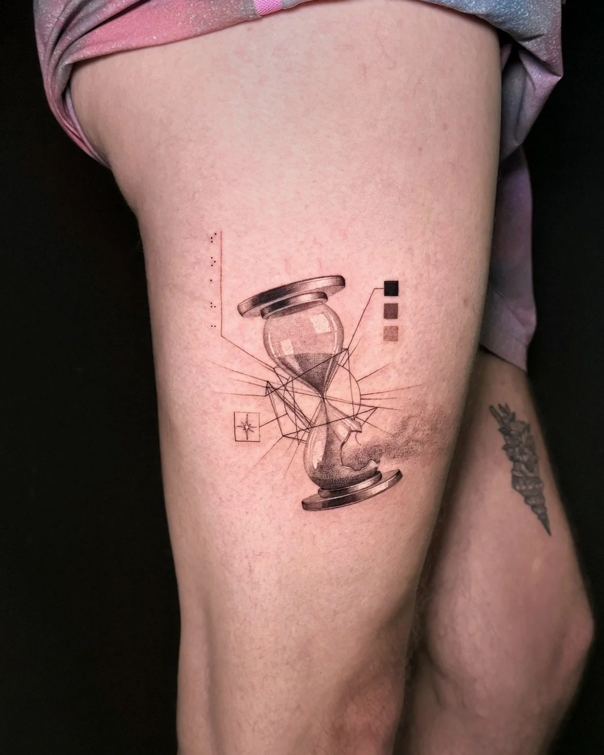 A hyper realistic tattoo done by Ihor (flowerhead.ink) on person's thigh. Featuring an hourglass with shattered glass and a birth chart around it.
