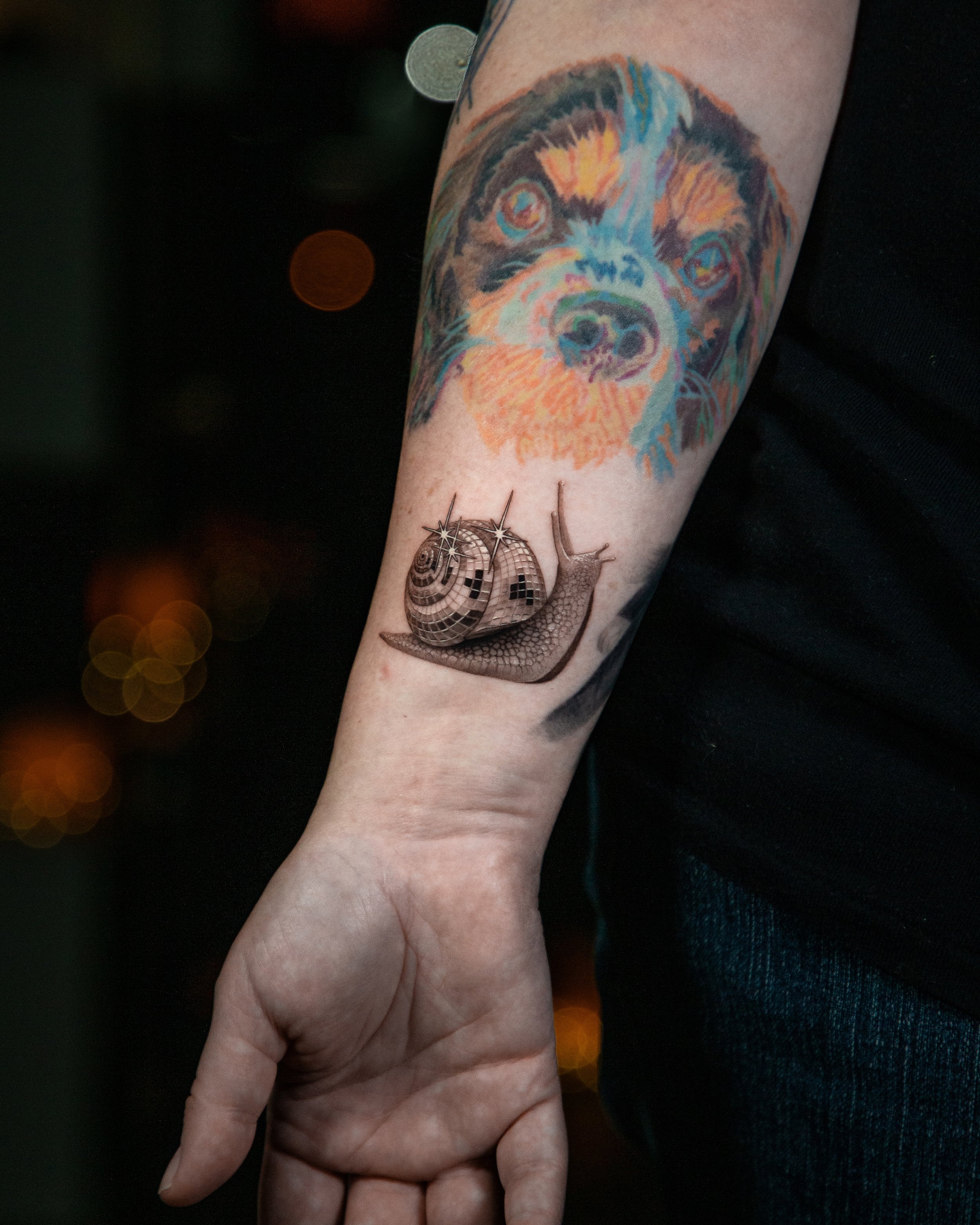 A hyper realistic custom tattoo done by Ihor (flowerhead.ink) on person's wrist. Featuring a  snail with a disco ball shell.