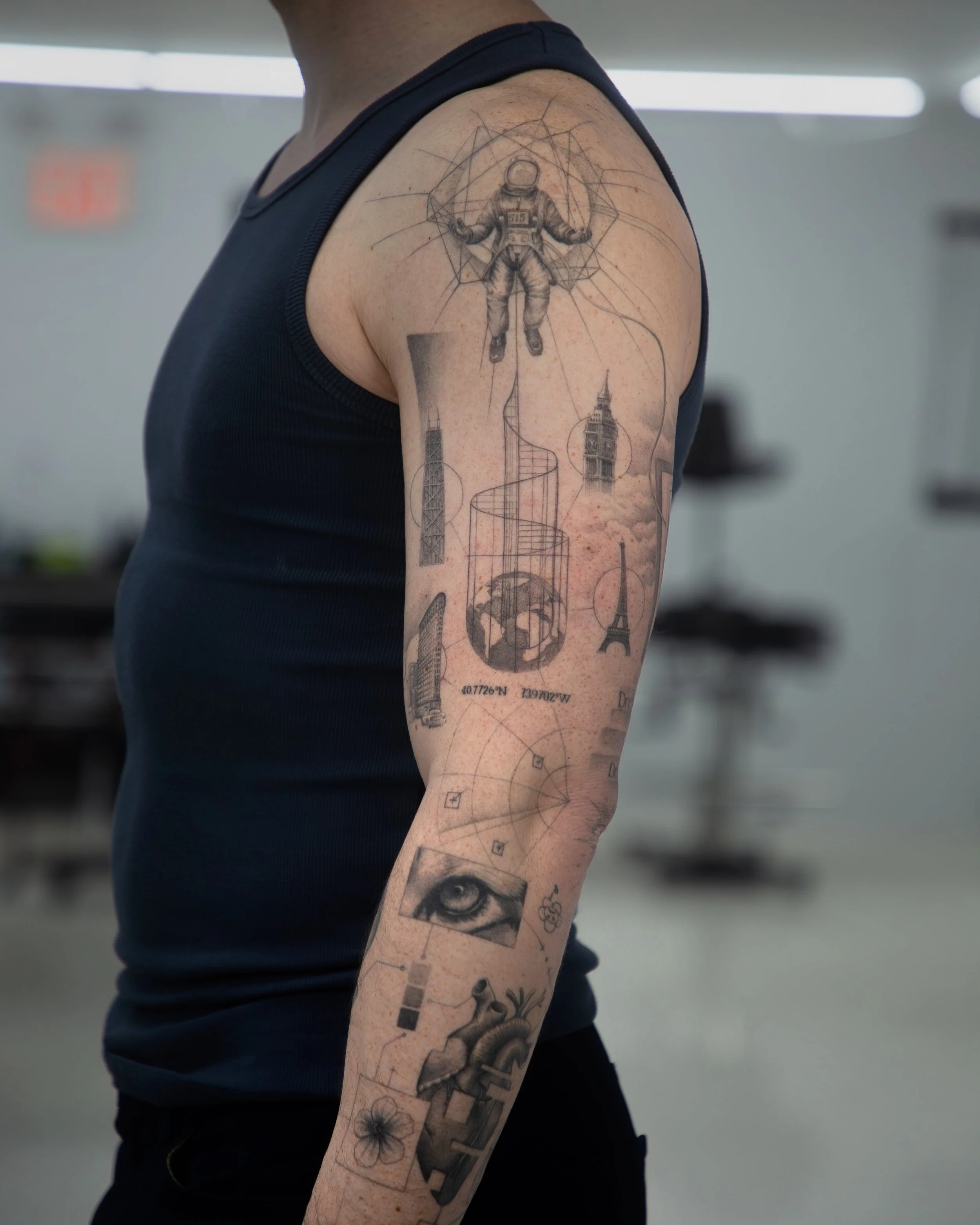 A hyper realistic sleeve done by Ihor (flowerhead.ink). Featuring an astronaut floating in space surrounded by his birth chart, with architectural landmarks, a planet Earth, tigers eye and other personal elements connected by clean fine lines. 