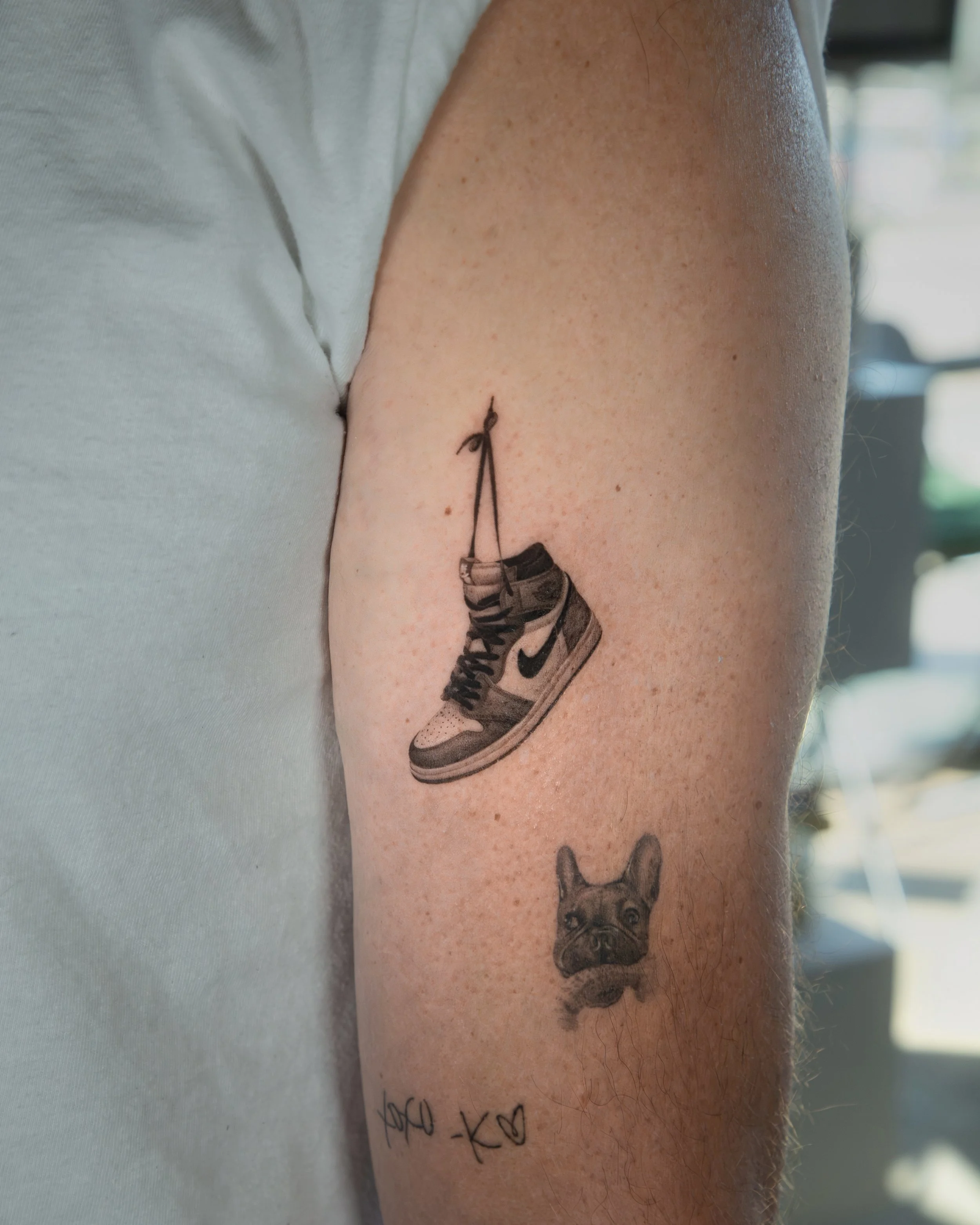 A tattoo by Ihor (flowerhead.ink) on a person's shoulder. Featuring a hyper realistic Nike shoe on the person's upper arm, tributing love to NYC and sneaker culture.