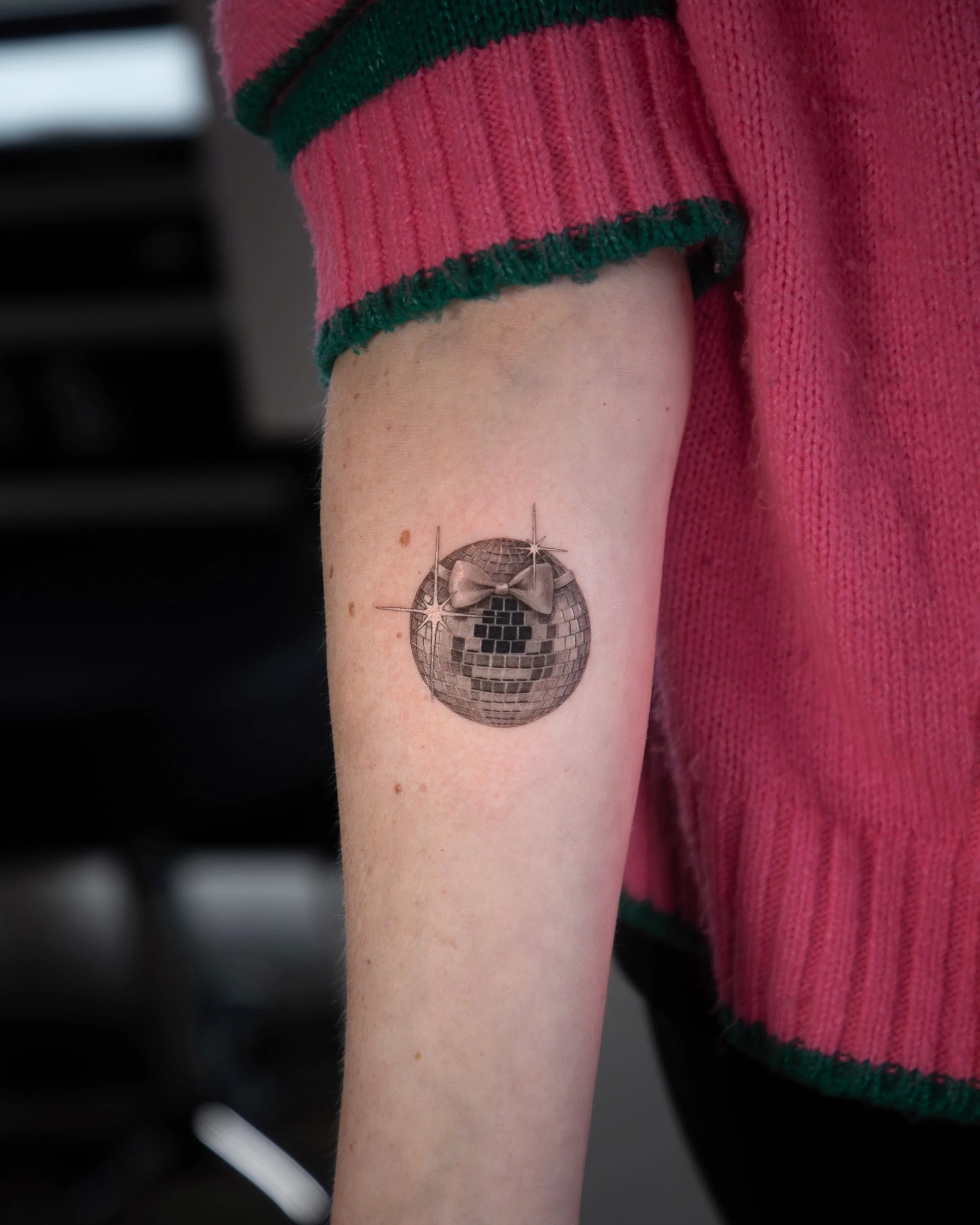 A hyper realistic tattoo done by Ihor (flowerhead.ink) on person's forearm. Featuring a perfectly shaped disco ball with a feminine bowtie on it. 