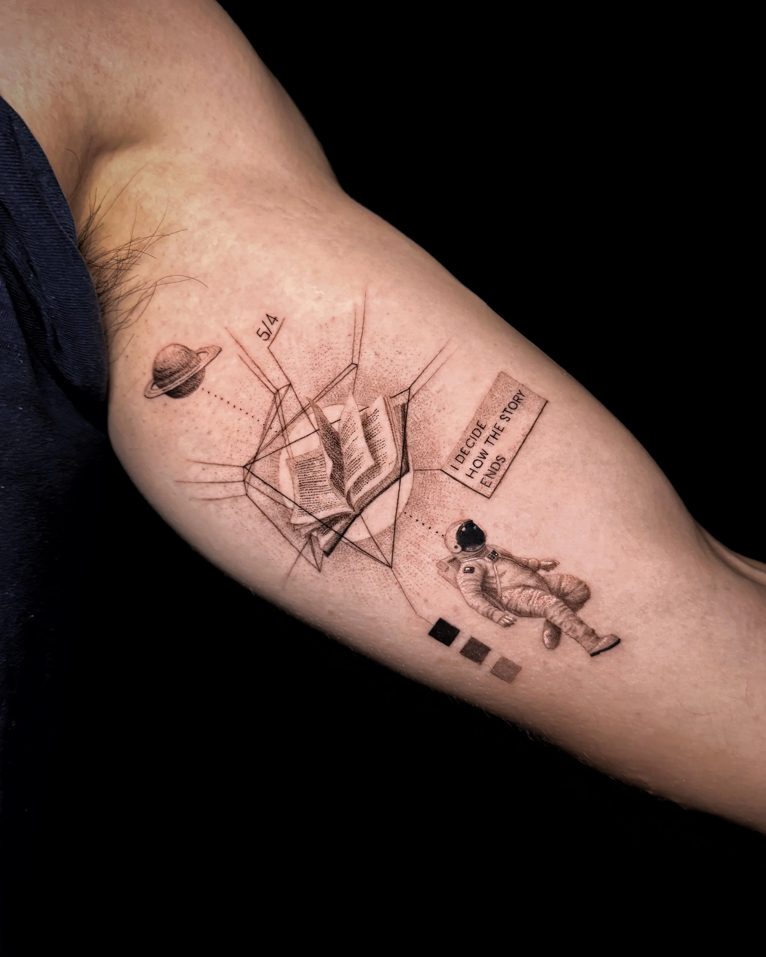 A hyper realistic tattoo done by Ihor (flowerhead.ink) on person's triceps. Featuring an astronaut, a Saturn, personal birth chart, a book inside it and a quote that reads "I DECIDE HOW THE STORY ENDS".