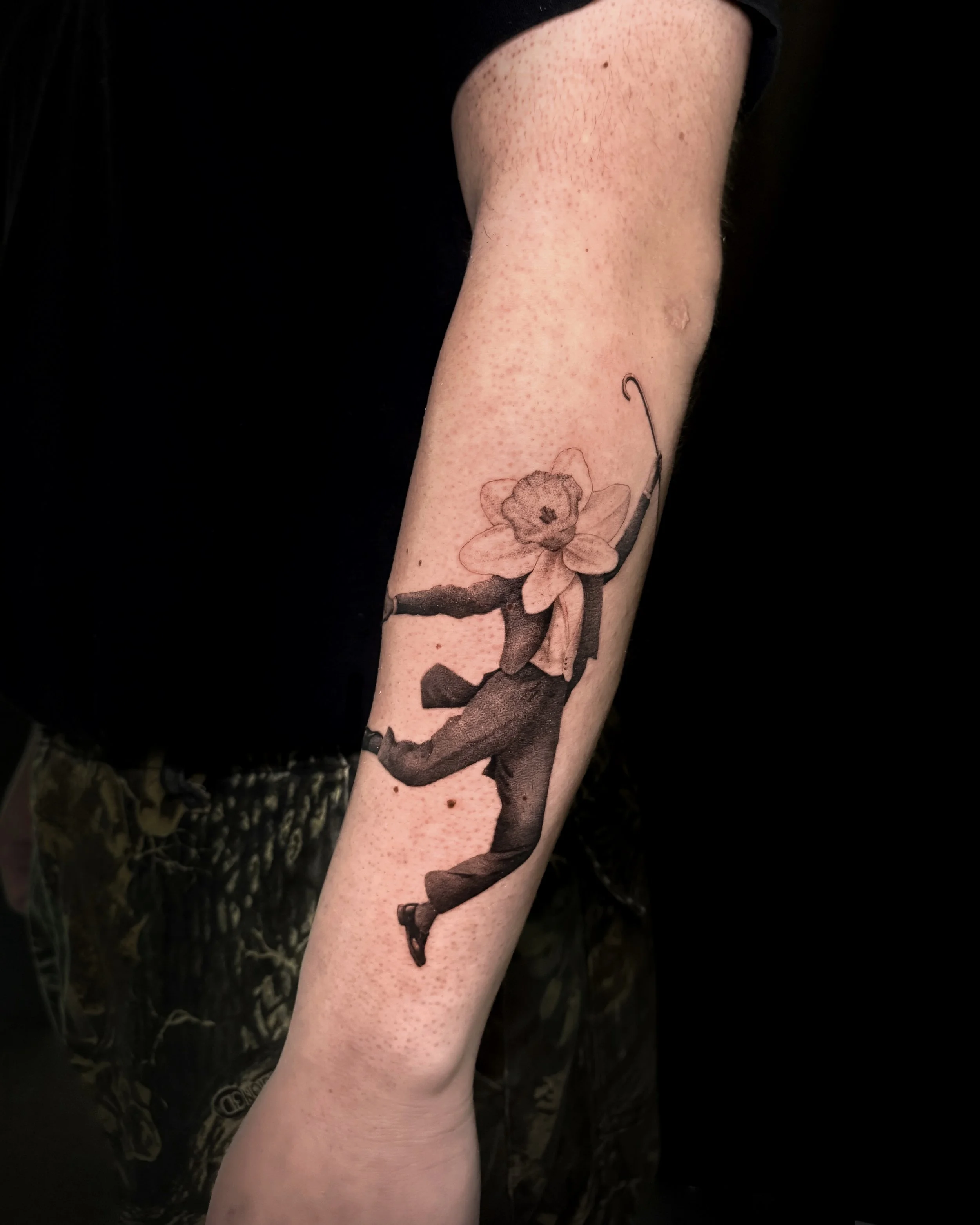 A hyper realistic tattoo done by Ihor (flowerhead.ink) on person's forearm. Featuring a dancer with a flower as a head (flowerhead), wearing a classic suit. 