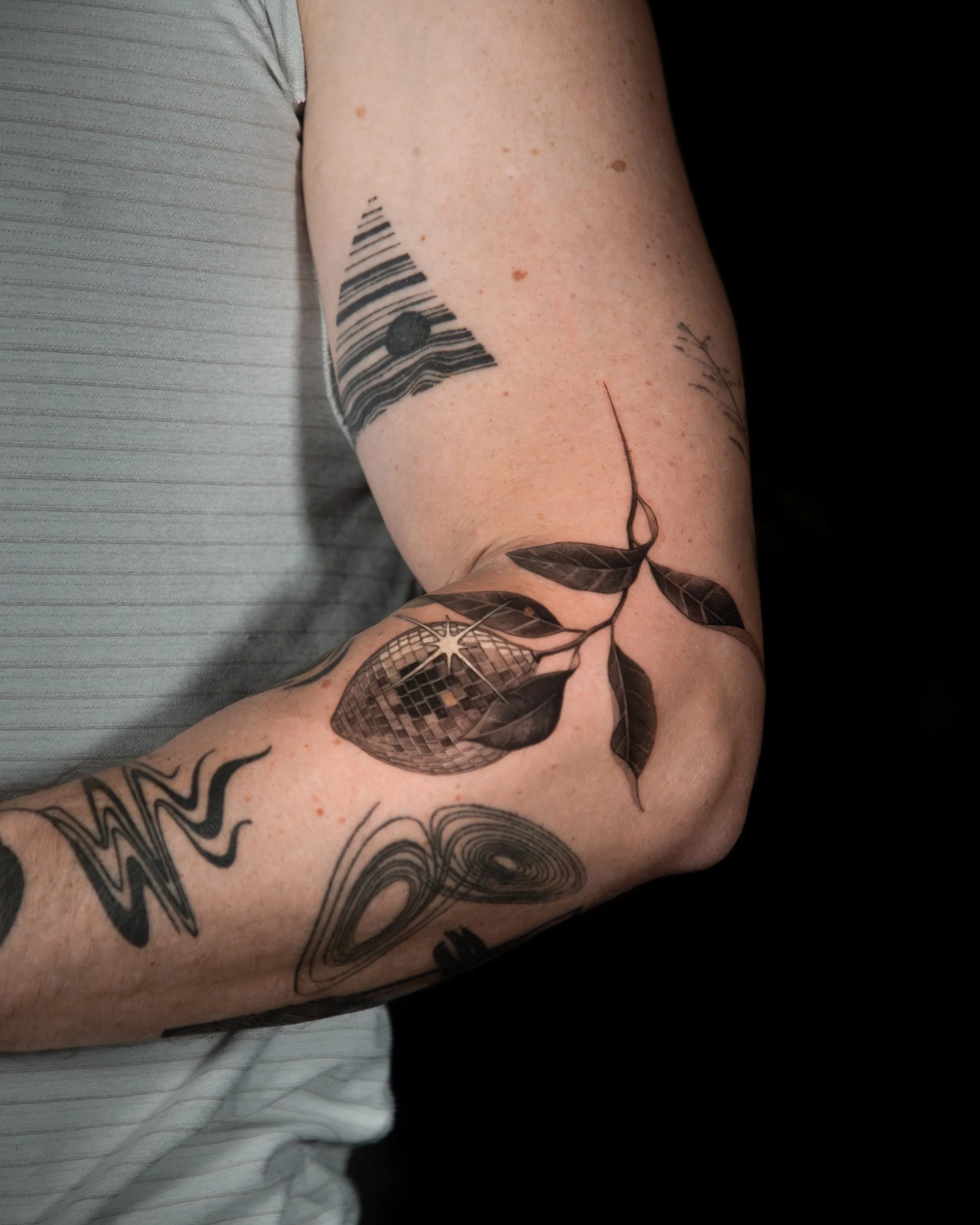 A hyper realistic tattoo done by Ihor (flowerhead.ink) on person's outer elbow. Featuring a disco ball textured lemon on a branch, placed on an elbow to compliment movement of the arm. 