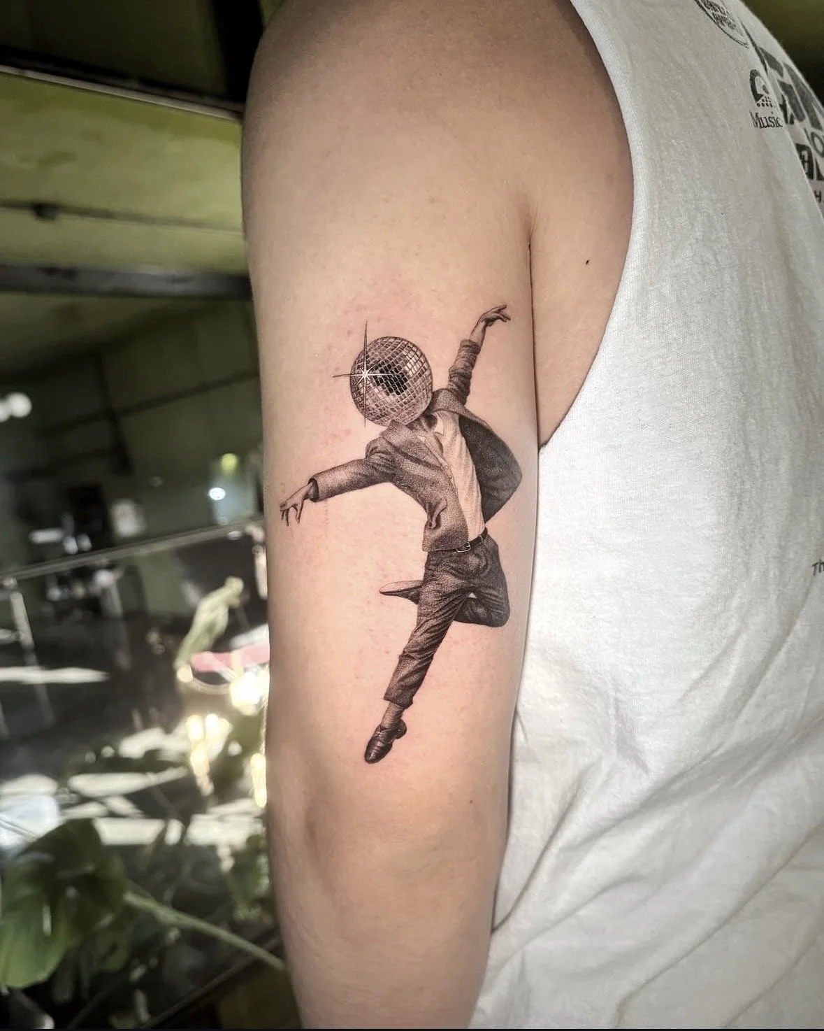 A hyper realistic tattoo done by Ihor (flowerhead.ink) on person's triceps. Featuring a dancing person with a disco ball for a head dancing in mid-air.