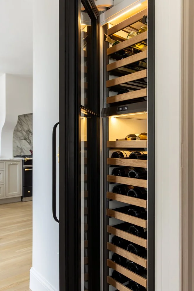 Tall modern built-in wine refrigerator with illuminated wooden racks filled with wine bottles beside a kitchen.