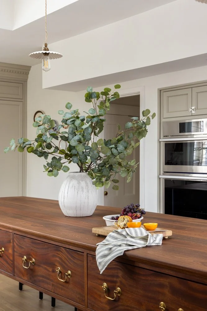 Elegant kitchen island with a white vase of eucalyptus branches, fruit platter, and striped dish towel