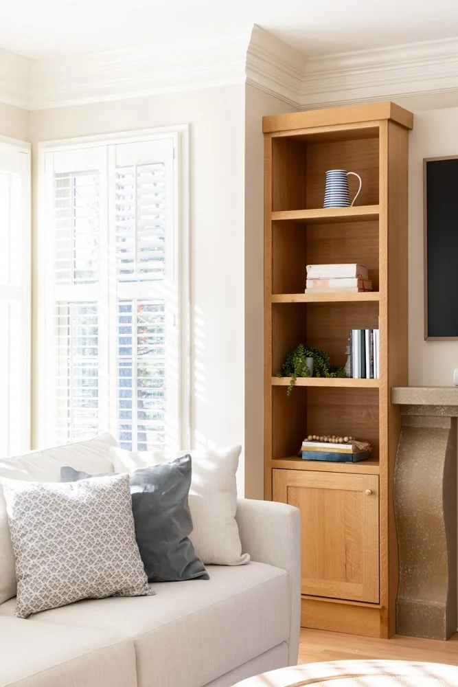 Bright living room with a white sofa, patterned pillows, wood bookshelf, striped pitcher, books, and fireplace mantel.