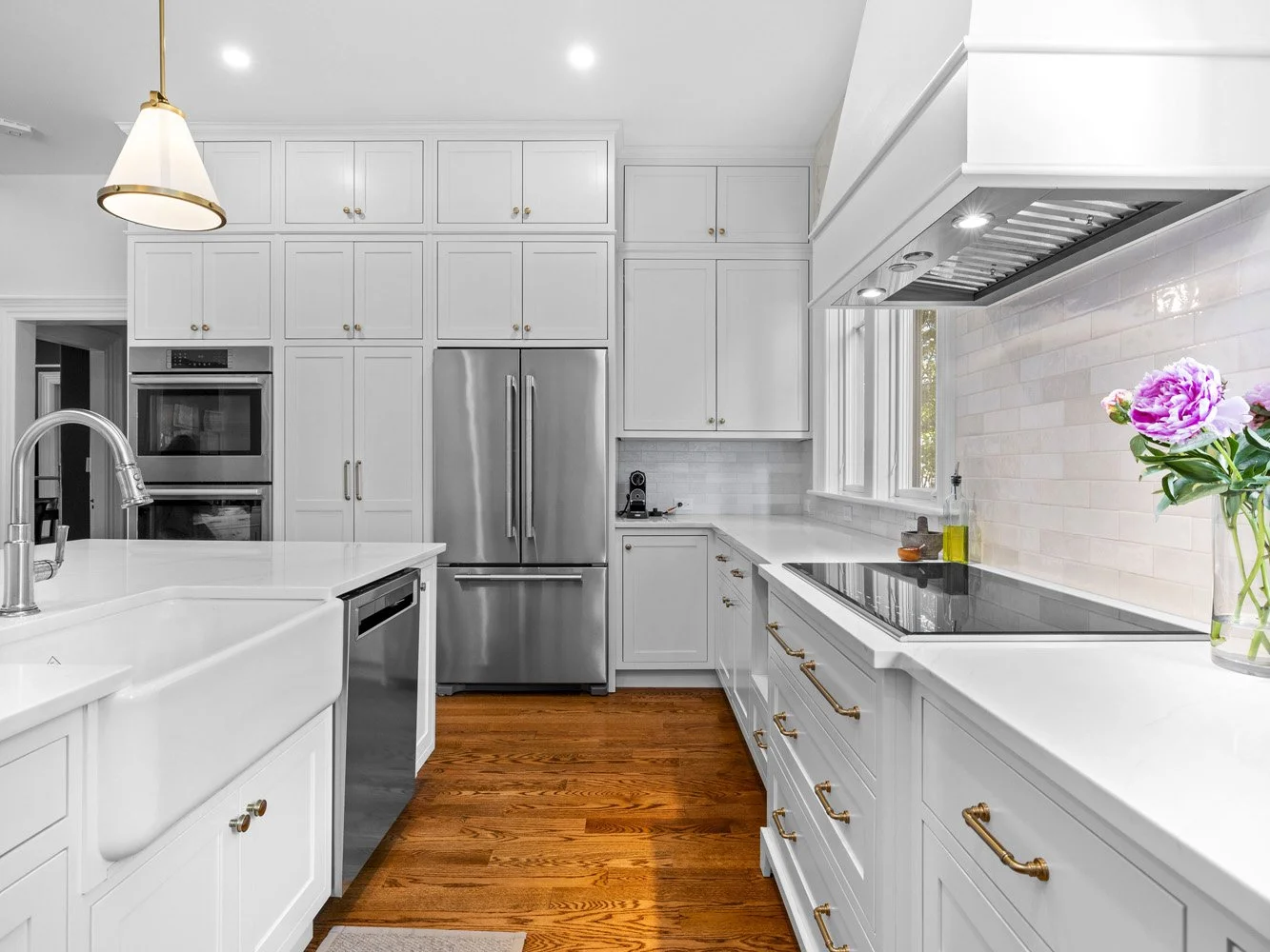 Bright white luxury kitchen with shaker cabinets, stainless steel appliances, farmhouse sink, marble countertops, subway tile backsplash, and hardwood floors