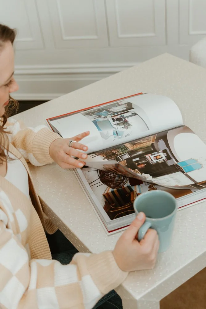 Woman holding a blue mug while flipping through an interior design magazine at a table