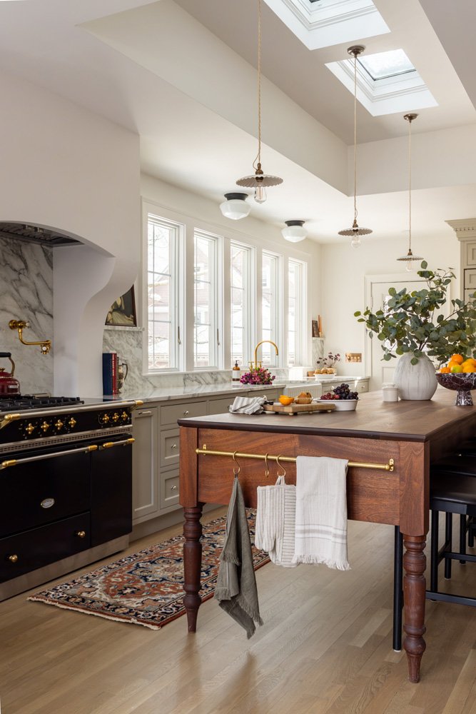 Bright traditional kitchen with a black range, marble backsplash, skylights, pendant lights, and a wood island topped with fruit and flowers