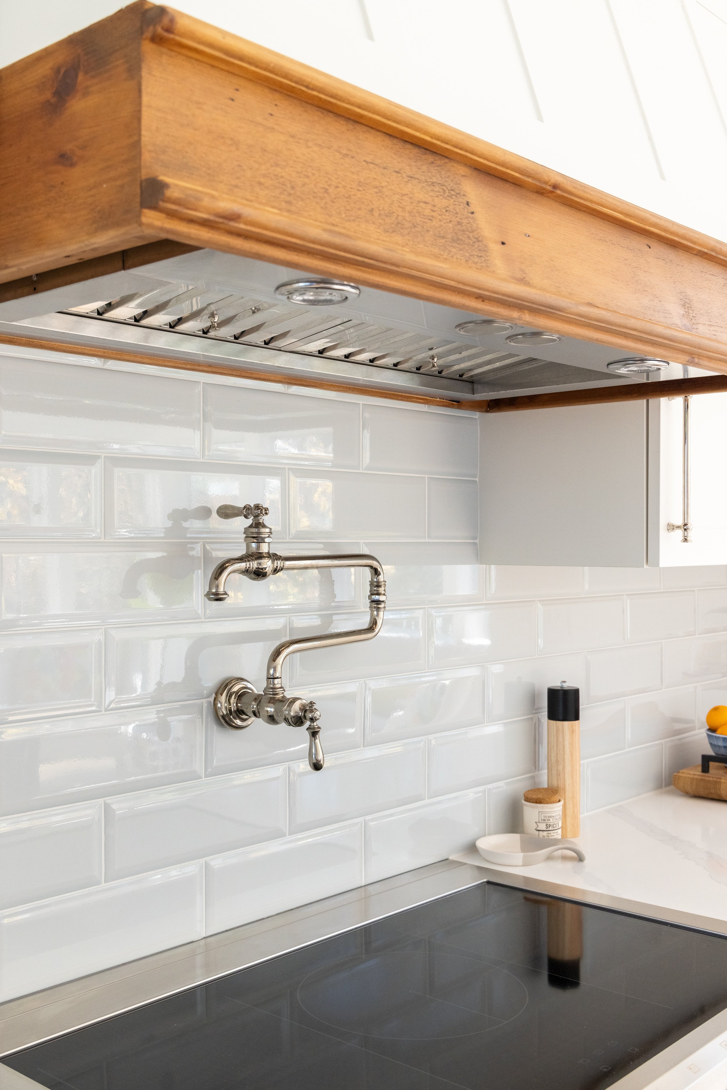 Bright kitchen with white subway tile backsplash, wood range hood, stainless pot filler faucet, and black induction cooktop