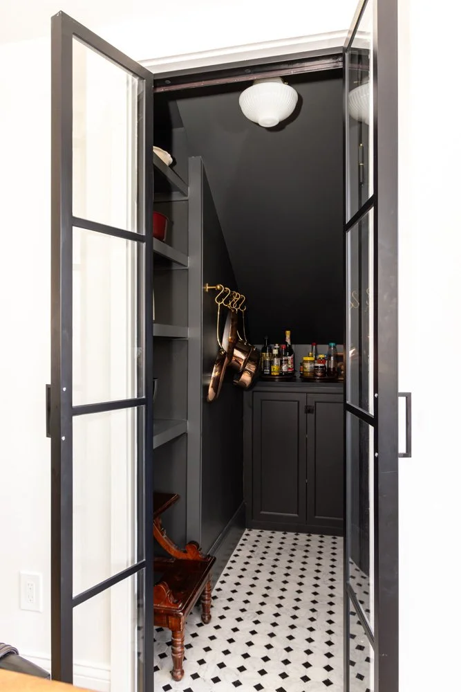 Elegant black butler’s pantry with glass doors, patterned tile floor, shelves, cabinetry, hanging handbags, and liquor bottles