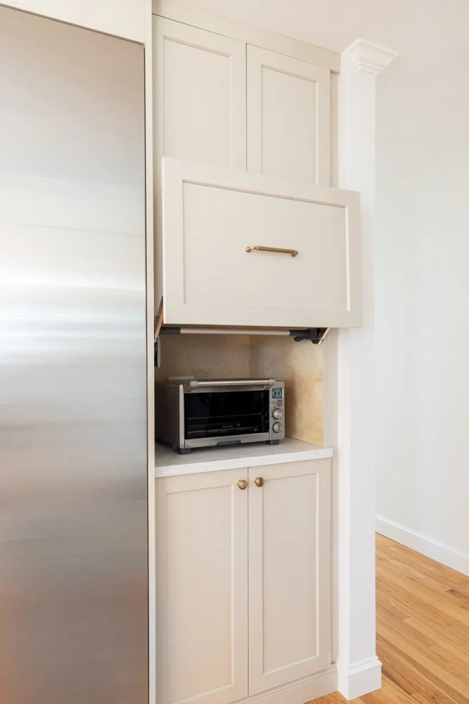 Built-in kitchen cabinet with a countertop toaster oven, cream paneled doors, and stainless steel refrigerator