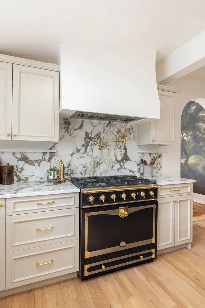Elegant kitchen with a black and gold range, white cabinetry, marble backsplash, and hardwood flooring