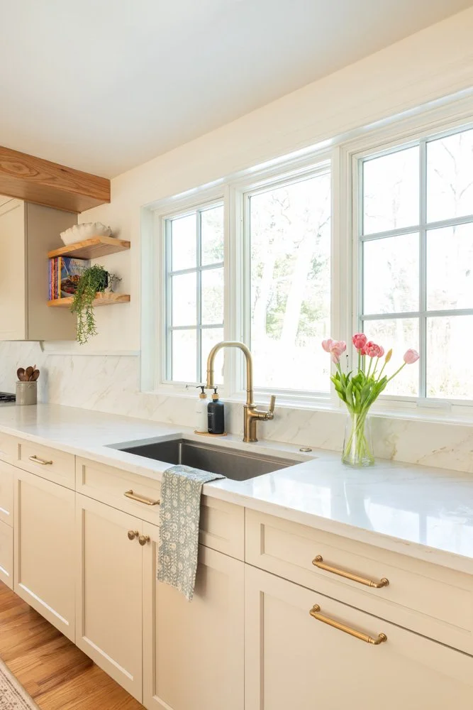 Bright farmhouse kitchen with white marble countertops, farmhouse sink, brass faucet, large windows, and pink tulips