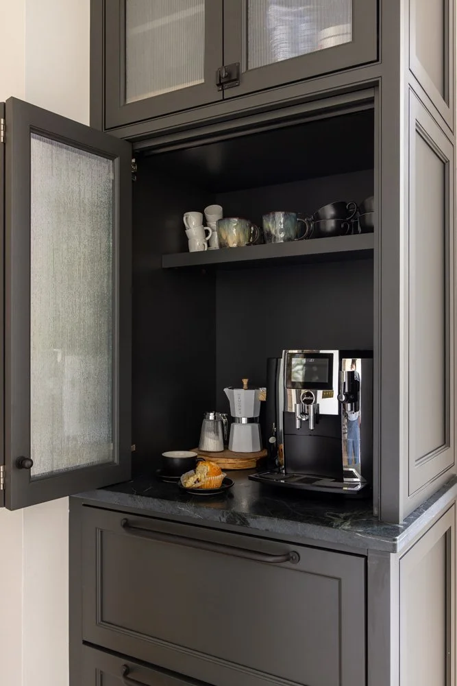 Built-in dark gray coffee bar cabinet with espresso machine, mugs, coffee accessories, and pastries