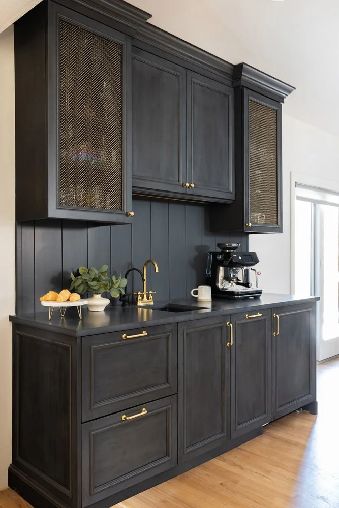 Custom black kitchen coffee bar with brass hardware, glass-front cabinets, espresso machine, sink, and wood flooring