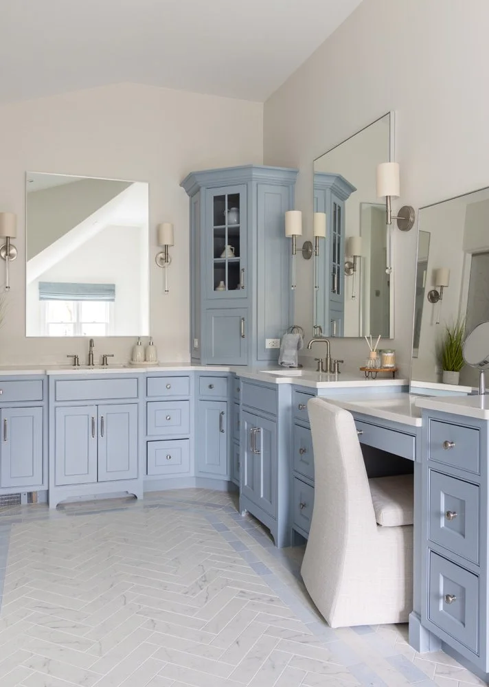 Elegant blue bathroom vanity with double sinks, built-in cabinet, large mirrors, sconces, and herringbone tile floor