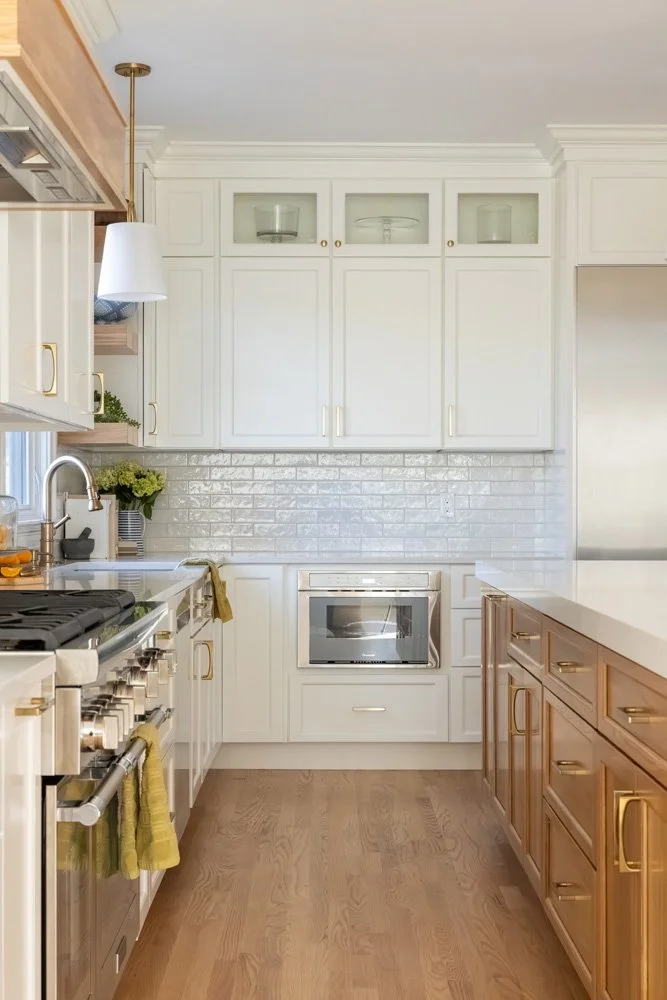 Bright modern kitchen with white cabinets, brass hardware, subway tile backsplash, stainless steel appliances, and wood flooring