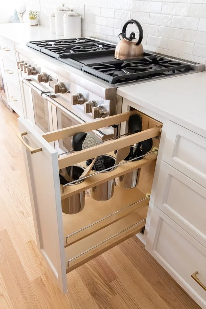 White kitchen with a gas range, copper kettle, and pull-out cabinet organizer storing pots, pans, and cooking utensils