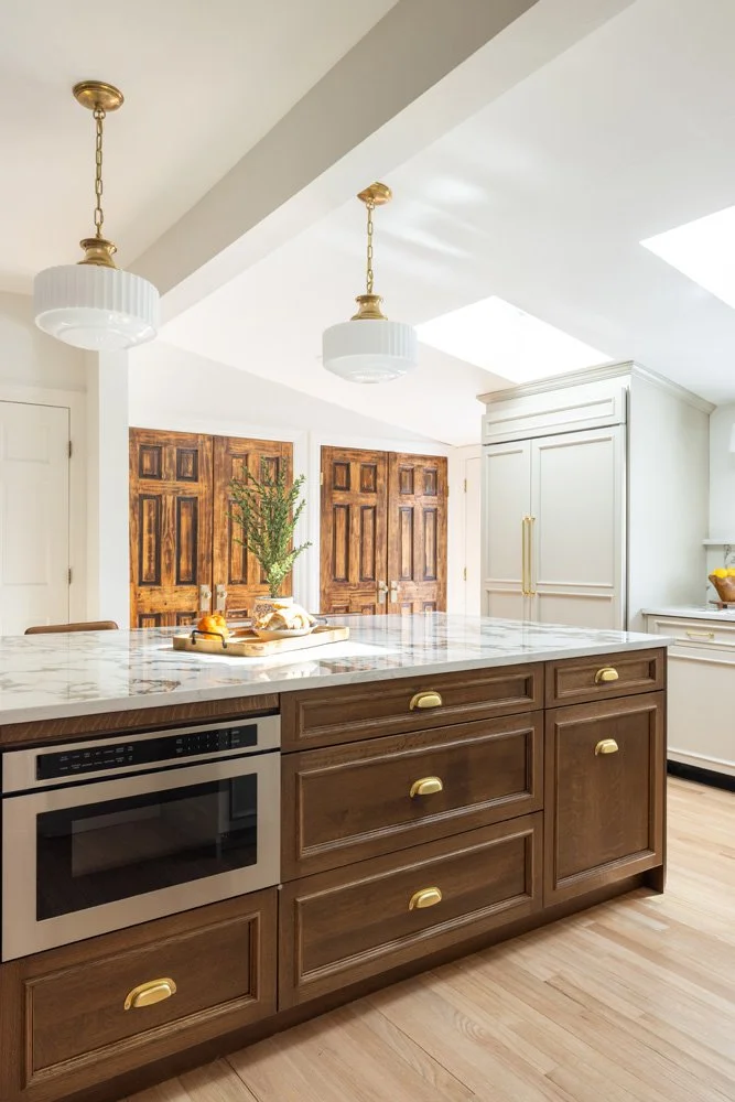 Bright traditional kitchen with a marble island, dark wood cabinets, brass hardware, pendant lights, and paneled wooden doors