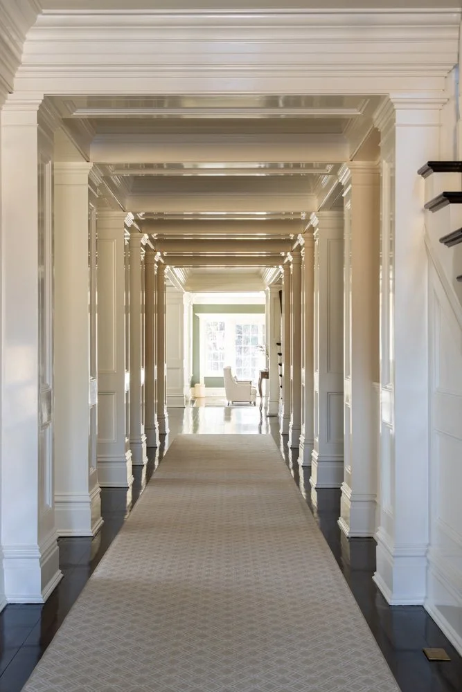 Elegant white-paneled hallway with repeated doorways, patterned runner, and bright sitting area at the far end