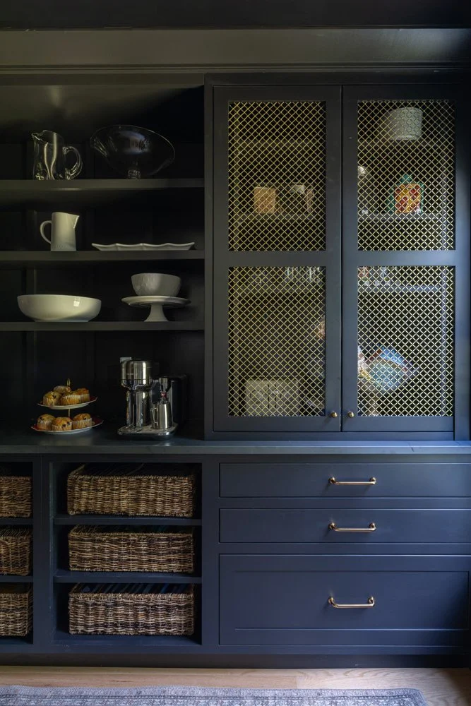 Navy blue built-in dining room cabinet with glass-mesh doors, white dishware, pastries, coffee accessories, wicker baskets, and drawers