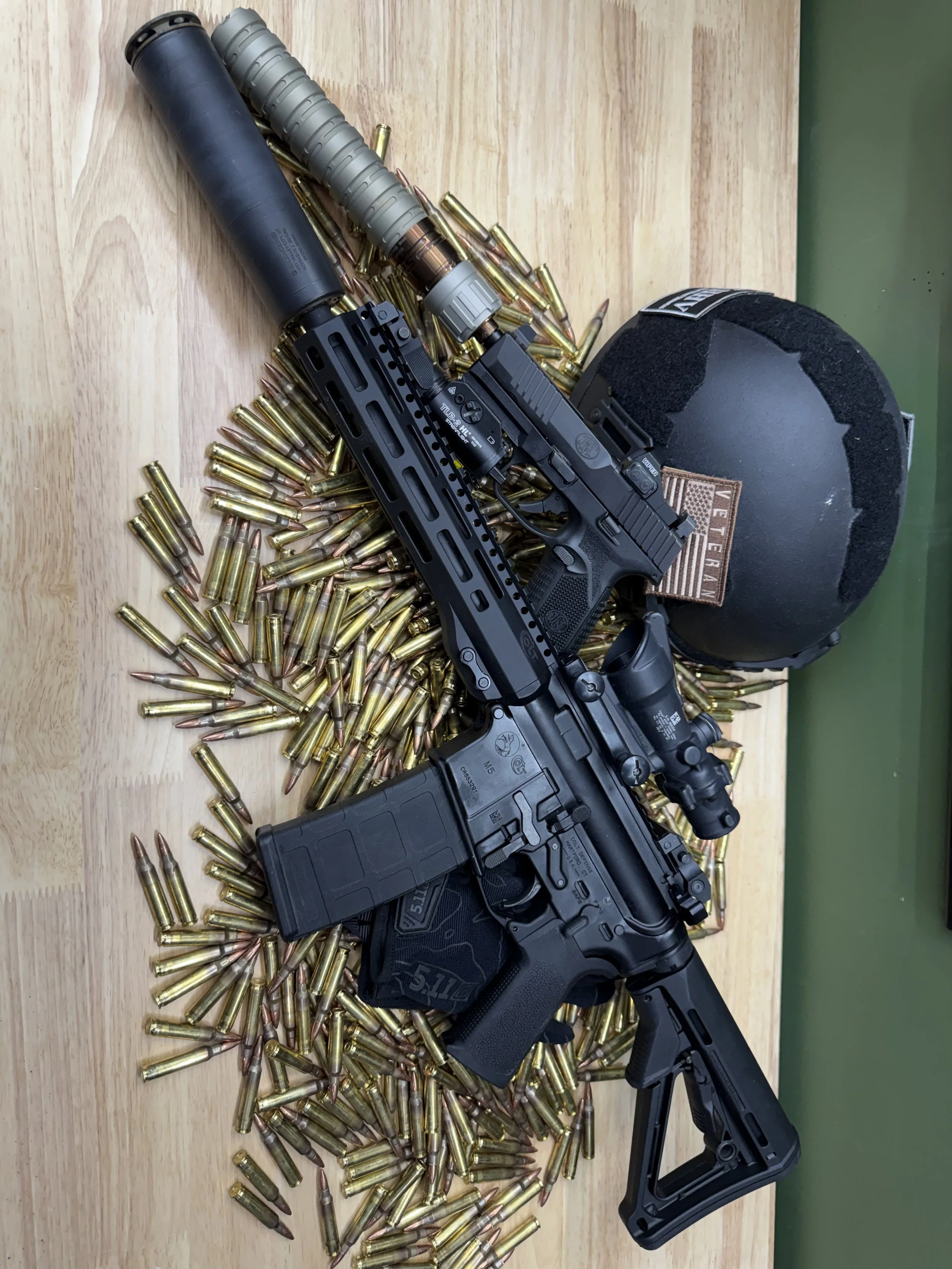 A handgun, a large number of bullets scattered on a wooden surface, a tactical flashlight, and a black helmet with a patch, with a green background.