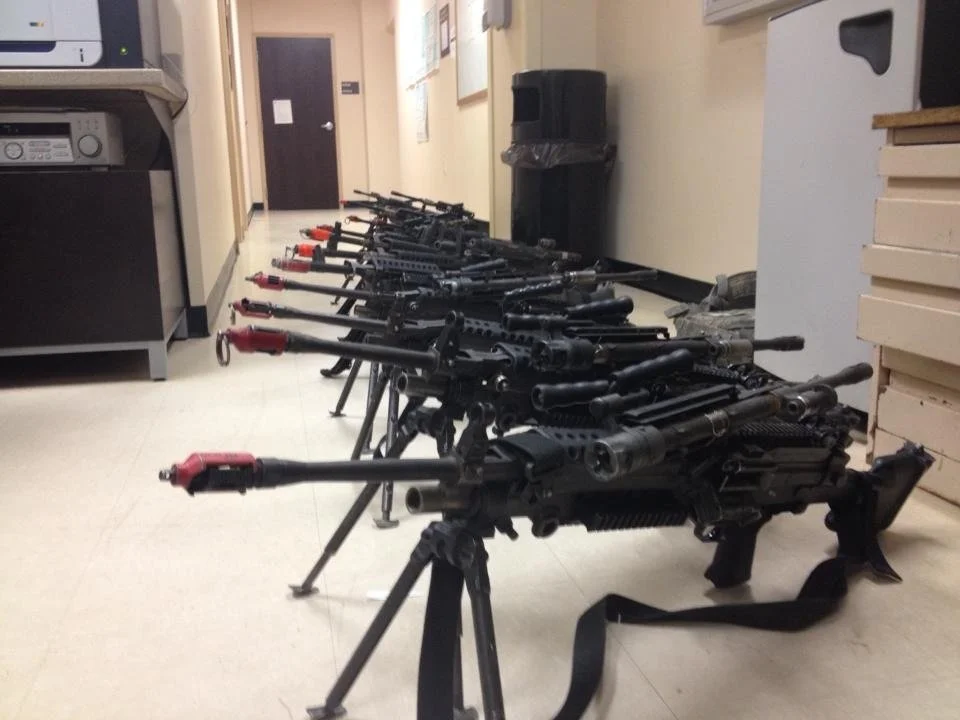 Multiple rifles with bipods lined up against a wall in a room.