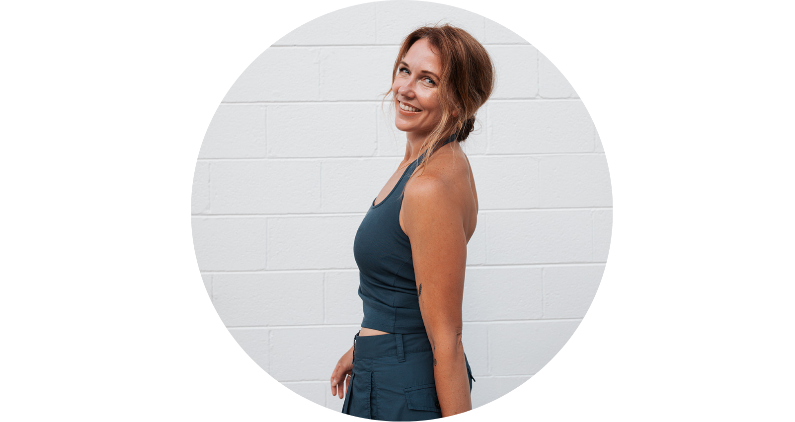 Woman with brown hair in a workout outfit smiling against white brick wall.