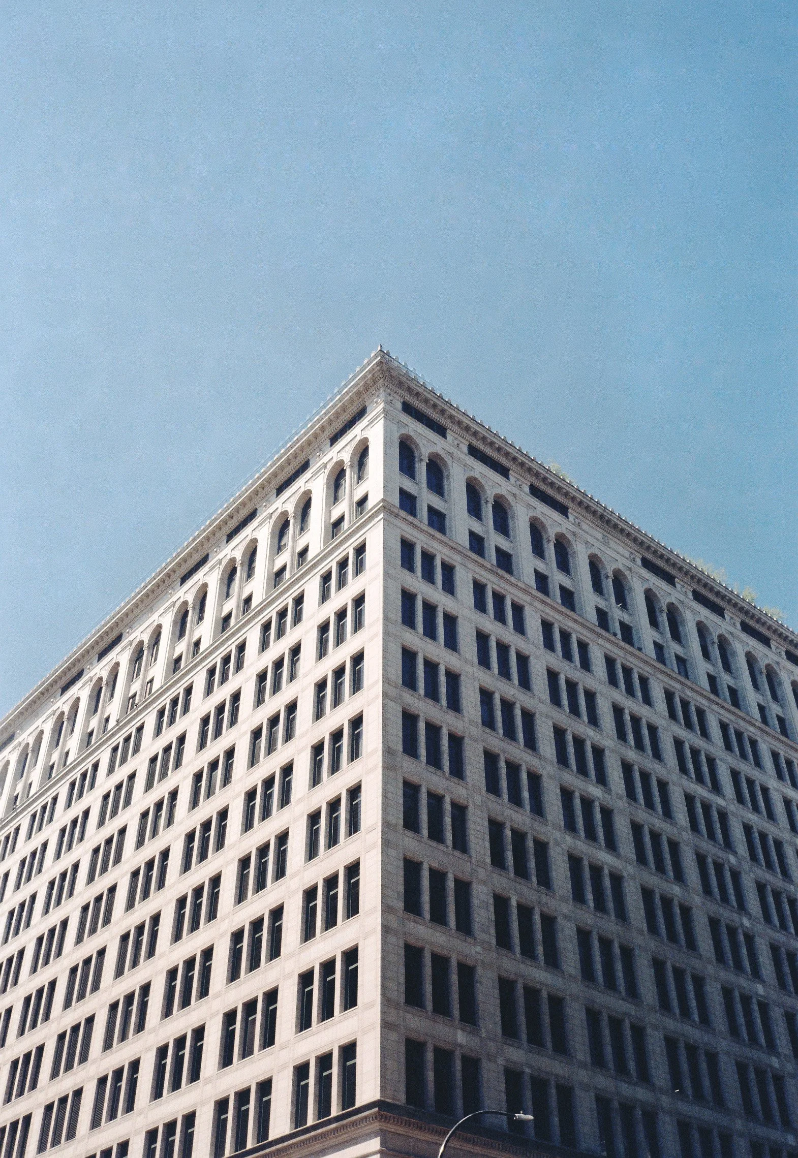 A tall, multi-story building with a white facade and many rectangular windows against a clear blue sky.