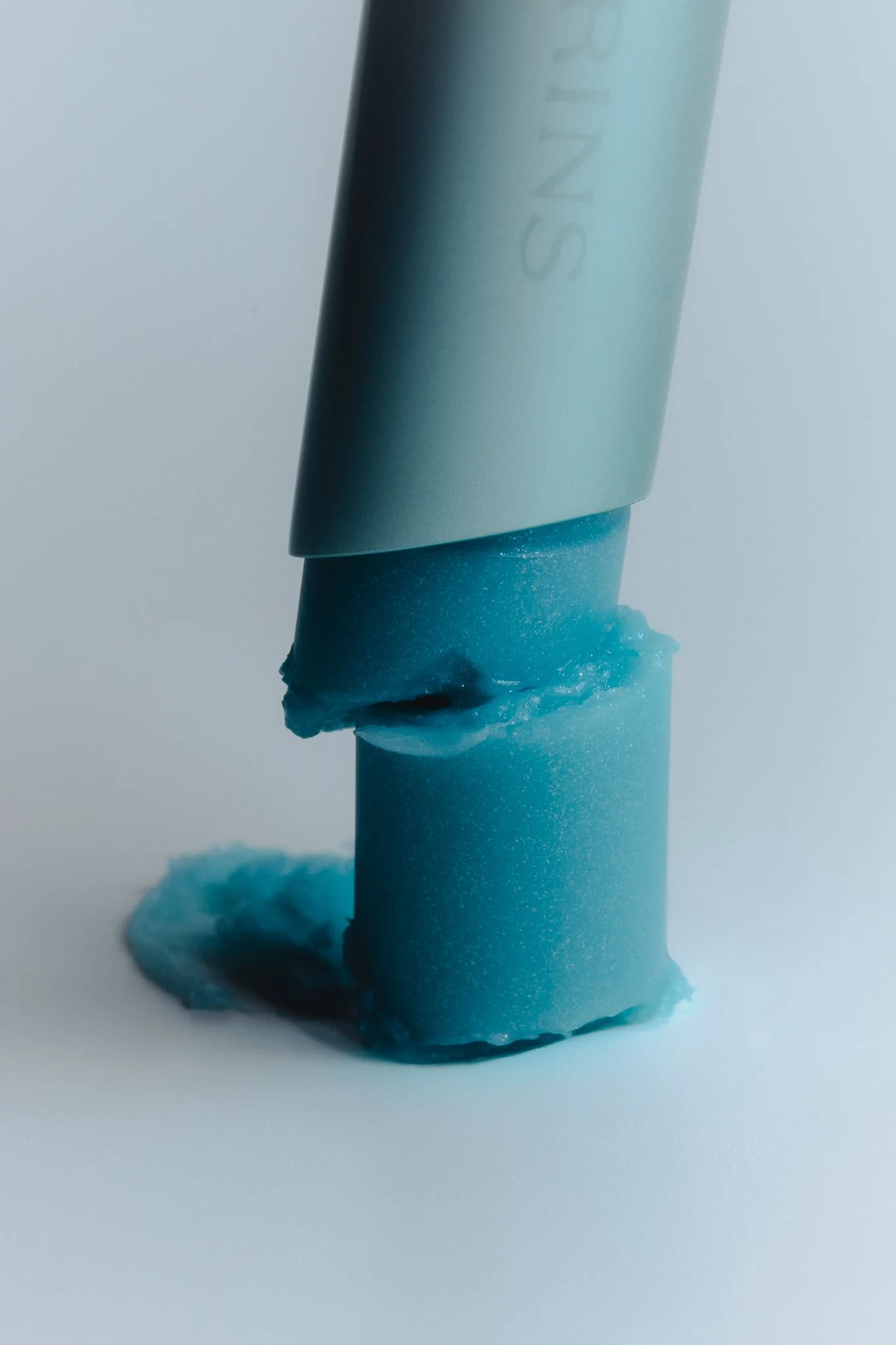 Close-up of a blue candle with a partially melted top, with a drip of wax around the base and a plain light background.