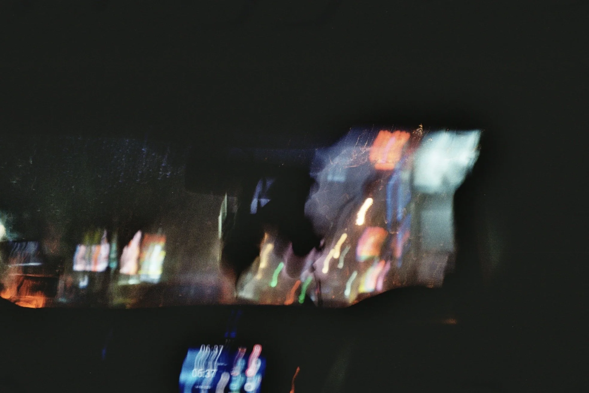 Blurred nighttime city street scene with colorful lights and reflections on wet pavement.