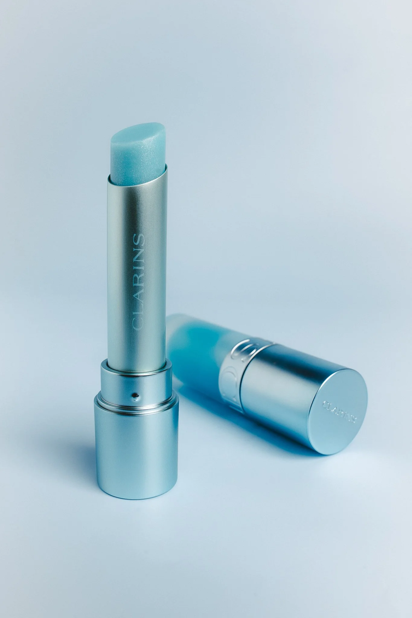 Two silver lipstick tubes with a metallic finish, one is open showing a blue lipstick, and the other is closed.