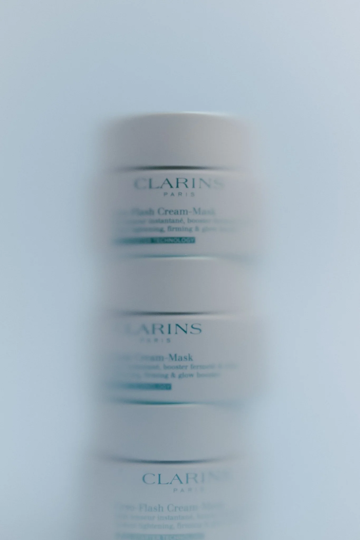 Blurry image of a jar of Clarins Paris moisturizer or face cream with a white lid.
