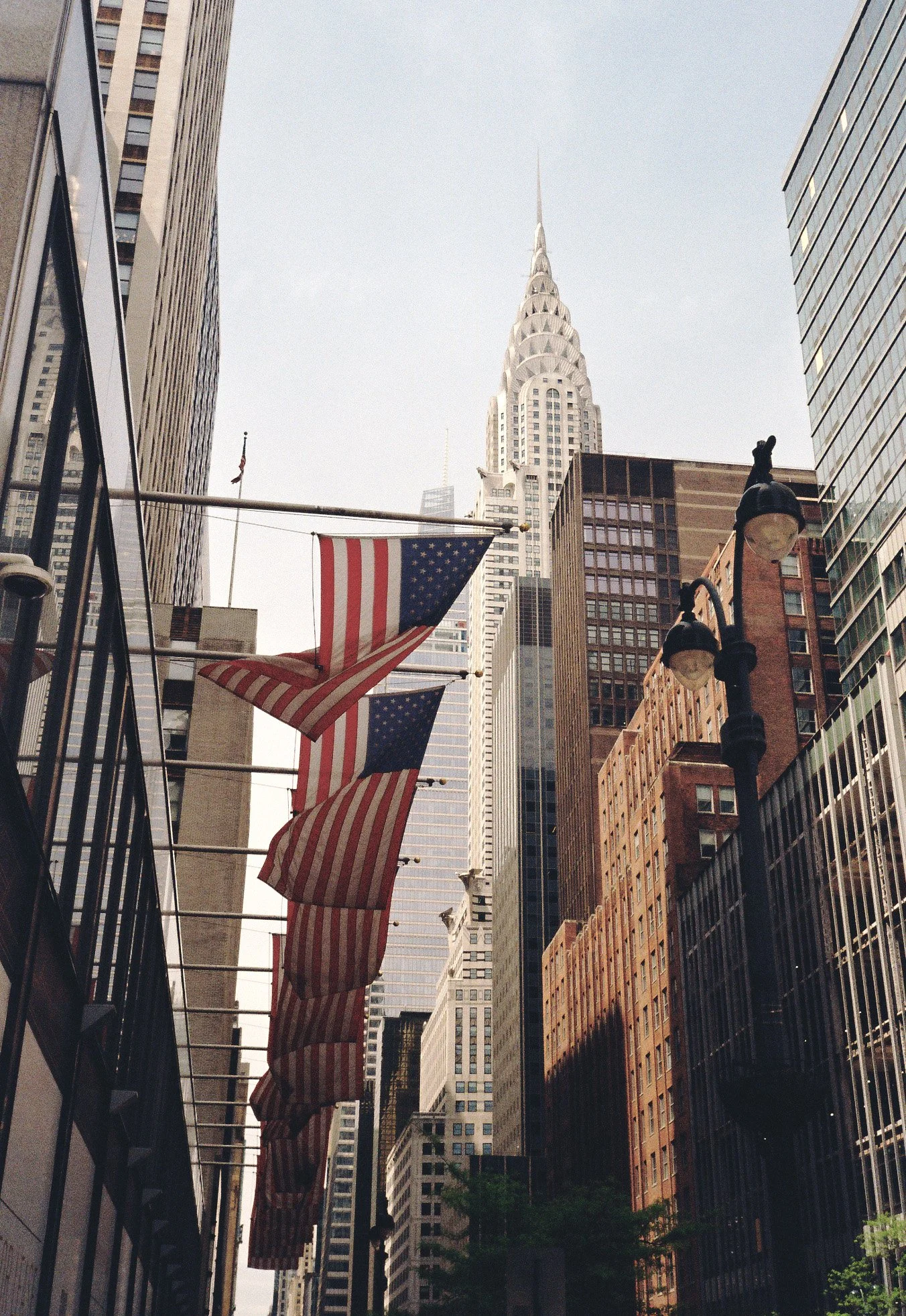 American flags hanging on a city street with tall buildings, including the iconic Chrysler Building in New York City.