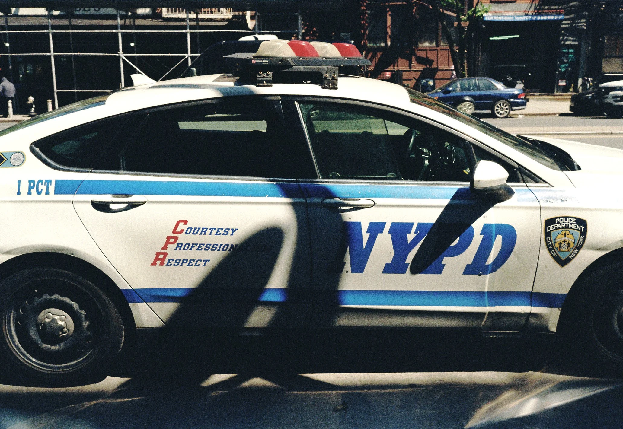 A New York Police Department patrol car parked on the street, with a city street and other cars in the background.