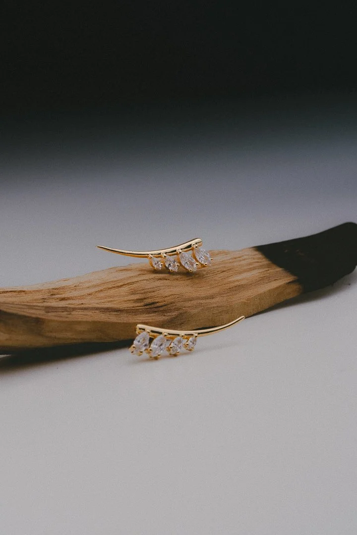Gold earrings with multiple clear gemstones on a piece of wood.
