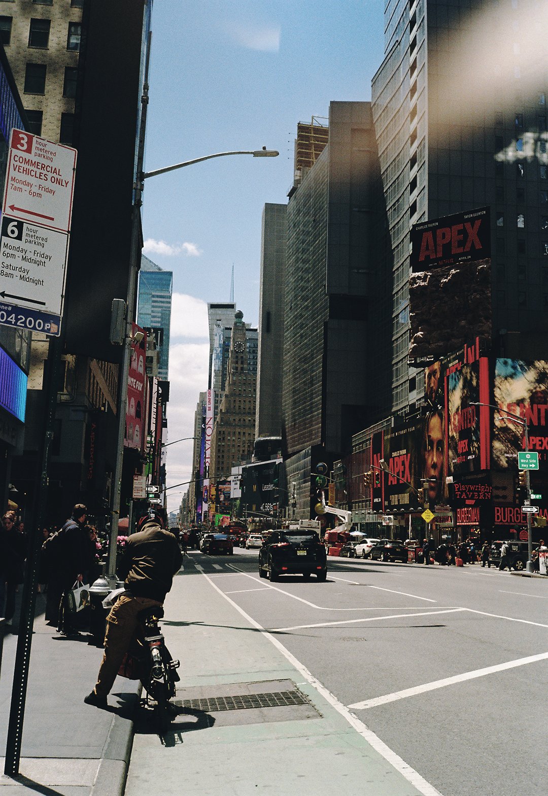 Street view in Times Square, New York City, with tall buildings, billboards advertising 'Apex', cars on the road, and pedestrians on the sidewalk.