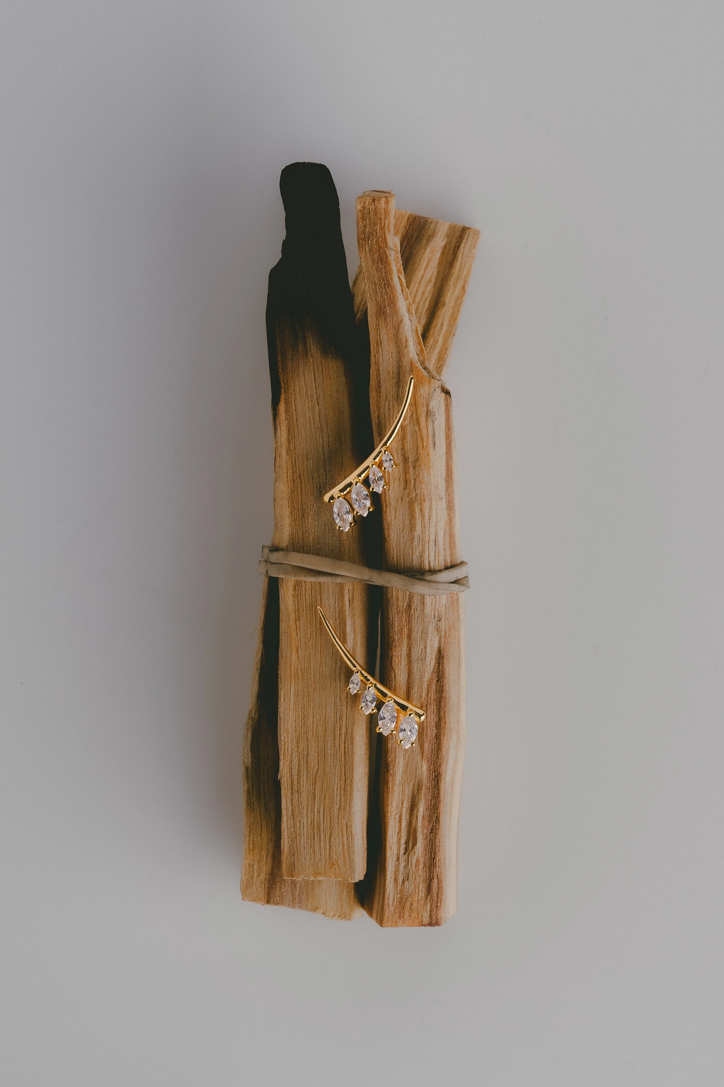 gold earrings with dangling clear gemstones hanging on a piece of wood against a plain background.