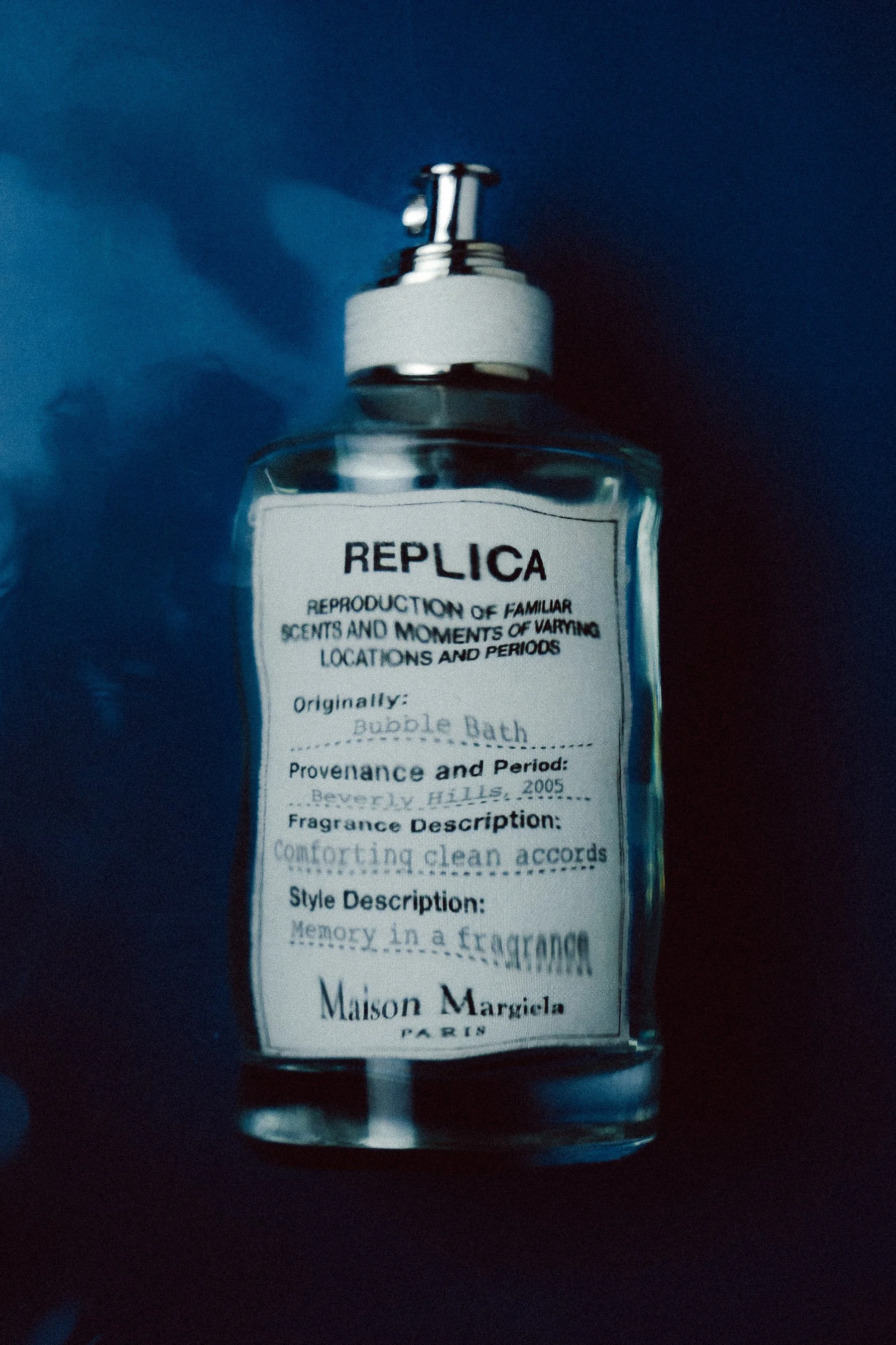 Close-up of a fragrance spray bottle labeled 'Replica' with details about its scent and origin, set against a dark background.