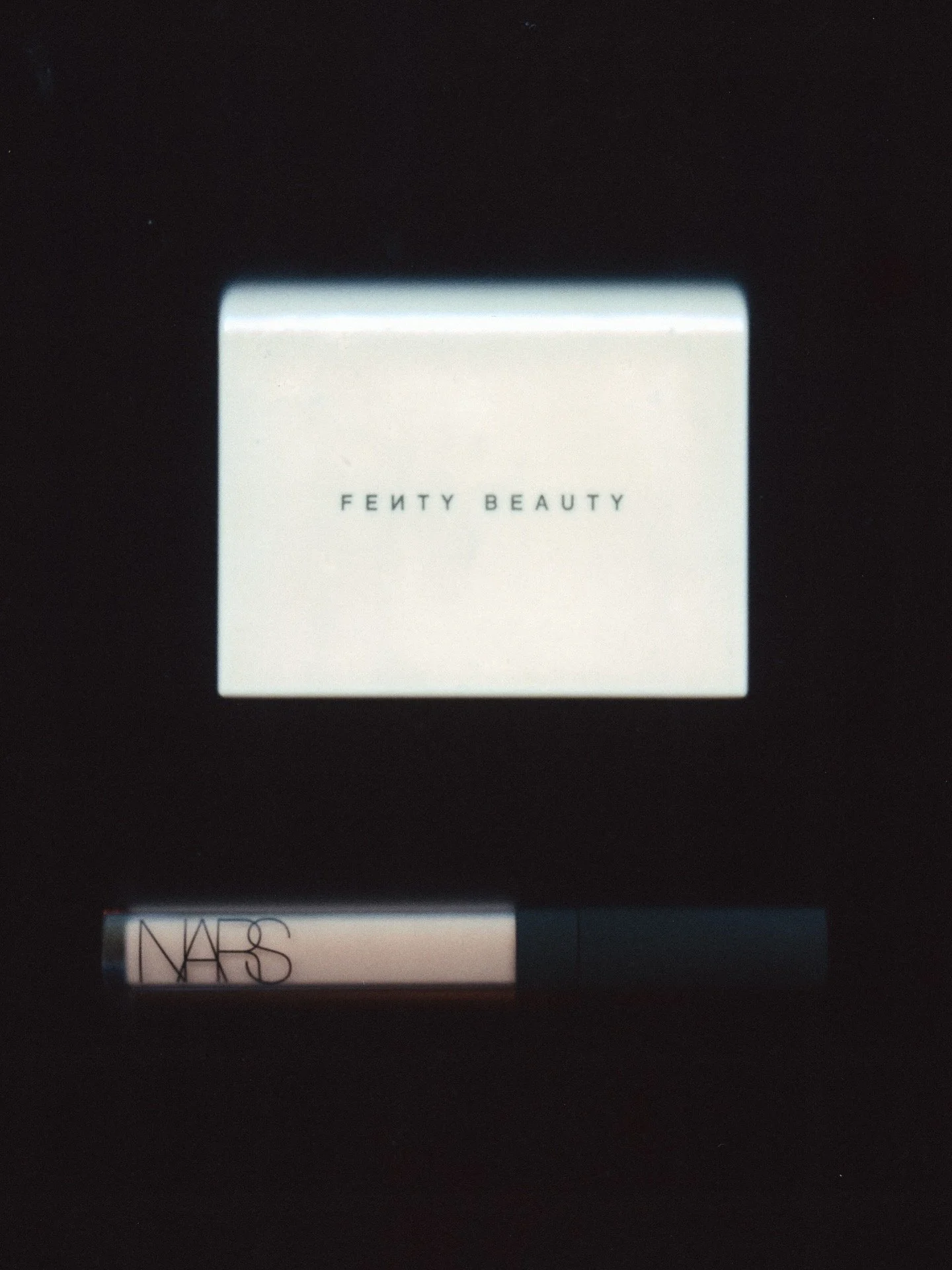 The image shows the logo of Fenty Beauty on a white box, with partial view of NARS makeup product below it.