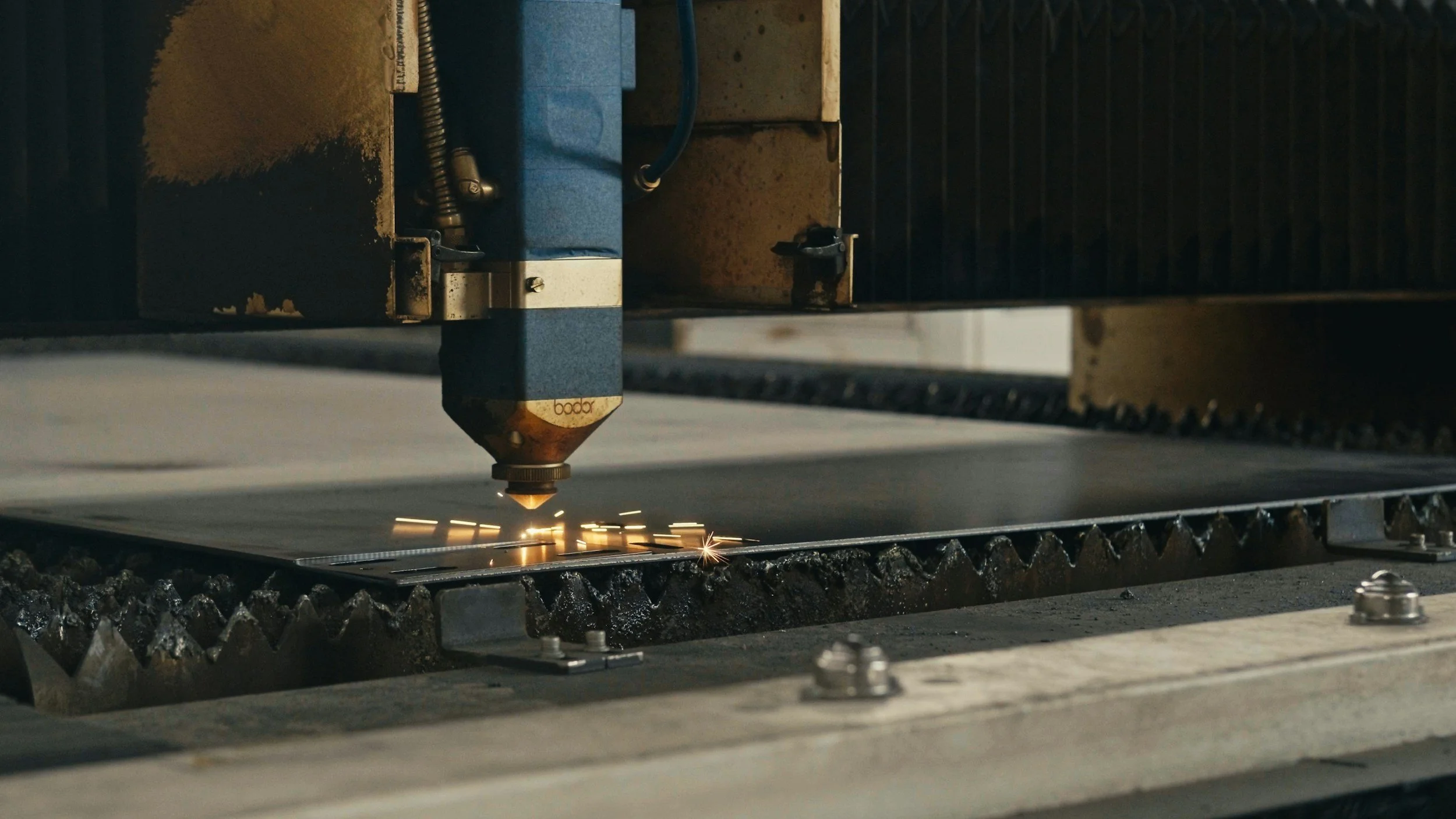 Close-up of a laser cutting machine engraving patterns onto a metal sheet, with sparks flying from the cutting process.