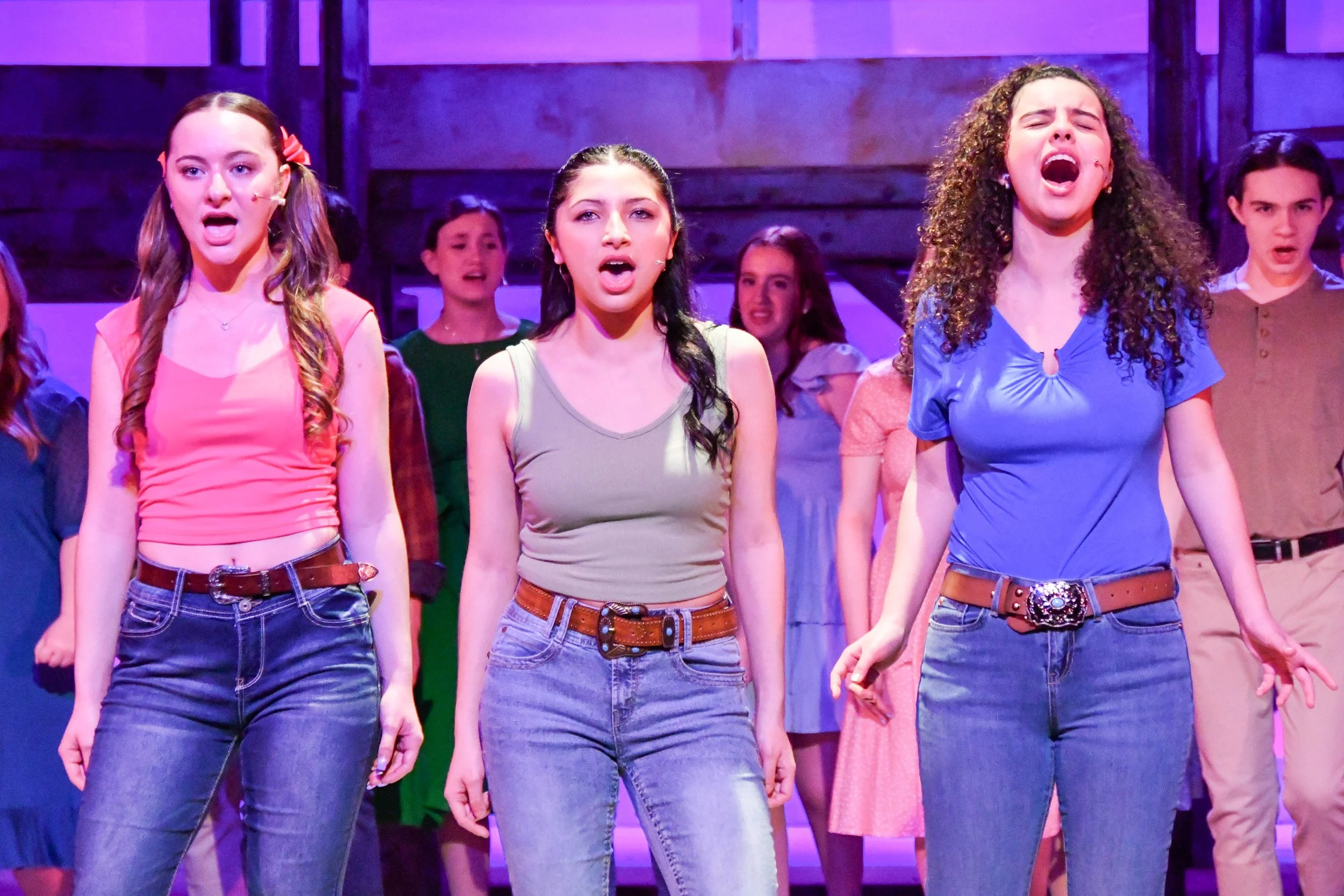 A group of teenage girls singing on stage during a performance, with expressions of emotion and engagement.