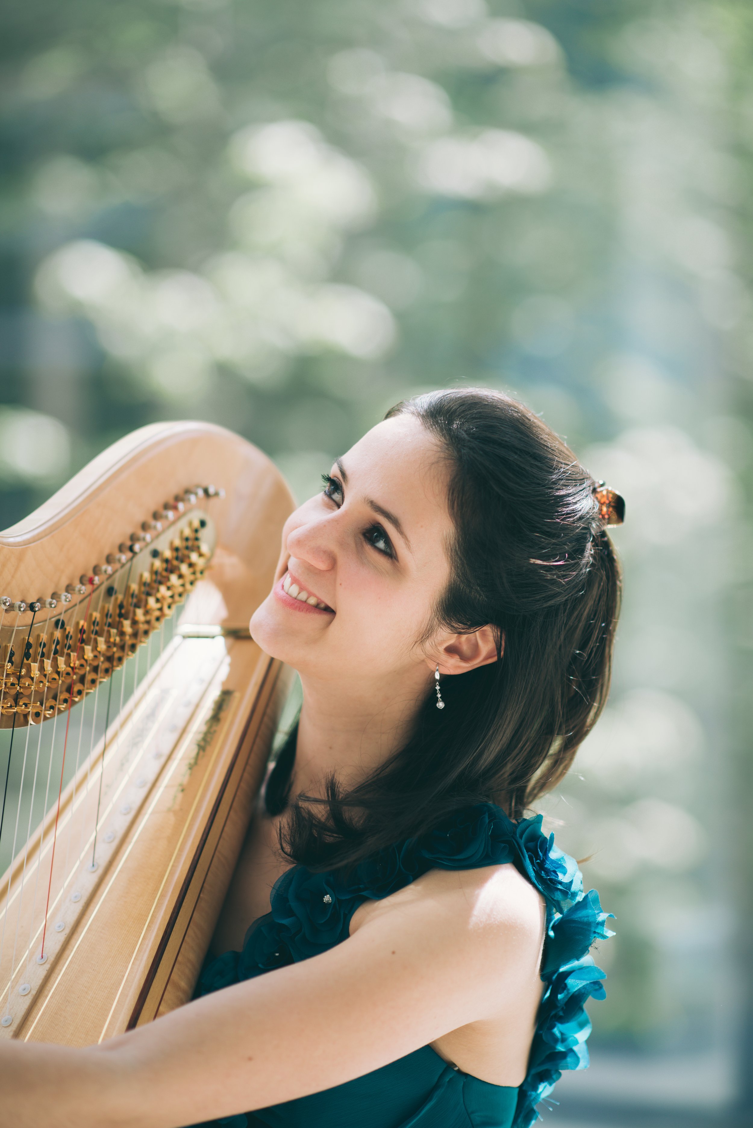 Sonia Bize, harpist, smiling while playing the harp outdoors in a teal dress