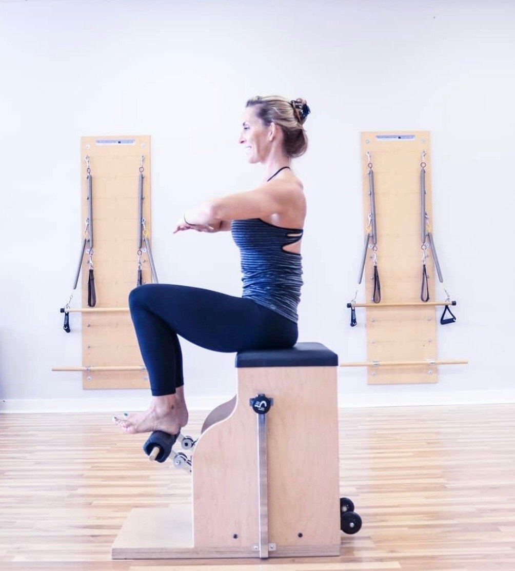 Nikki LaFord seated on an exercise bench performing a Pilates movement near wall-mounted resistance bands