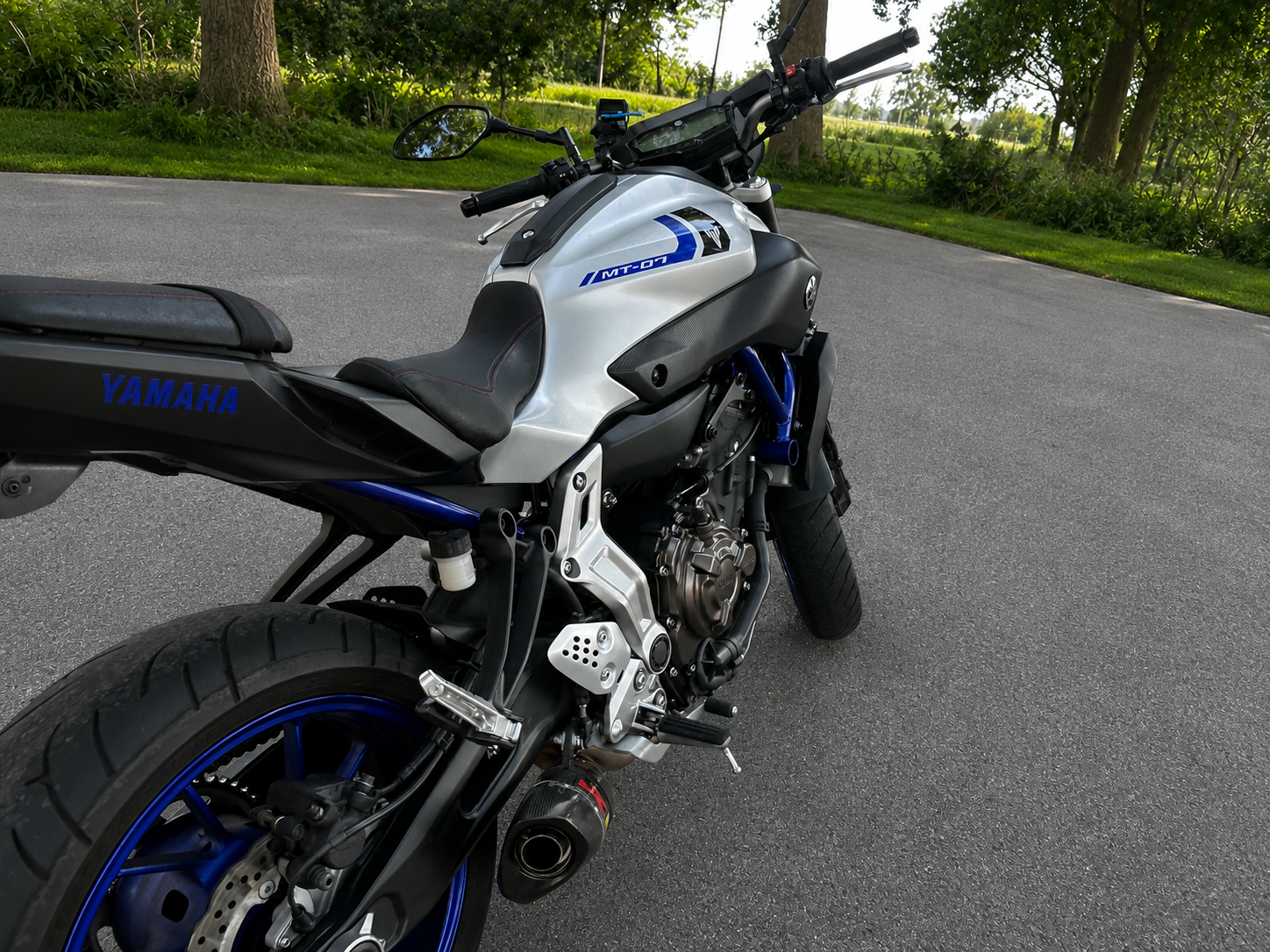 Een Yamaha MT-07 motorfiets op een rustige asfaltweg, omringd door groene bomen en struiken.
